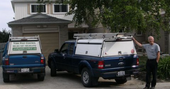 The original owner of York Pest Control beside two small blue trucks with white cabs.